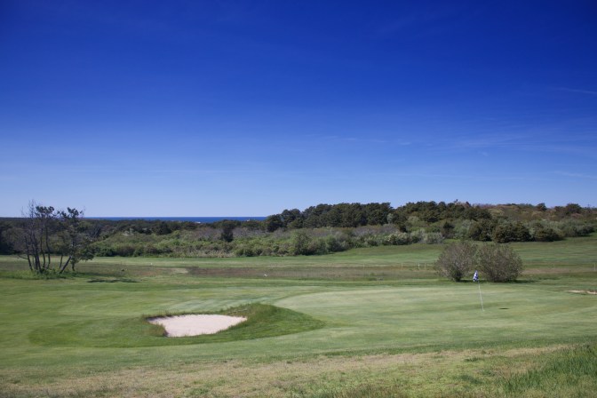 Golf course sand trap and hole, with ocean in the distance.