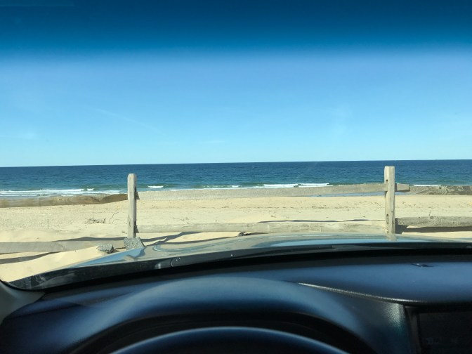 View of ocean and beach through car windshield.