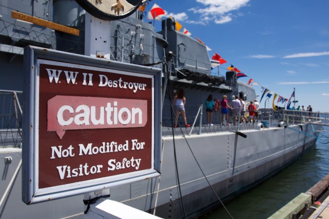 Sign that says "WWII Destroyer CAUTION Not Modified for Visitor Safety" in front of ship.