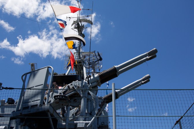 Looking upward at anti-aircraft guns and ship's mast.