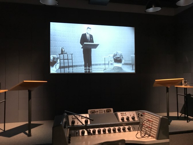 Mockup of TV studio. A screen in the background is projecting the first Presidential debate of 1960.