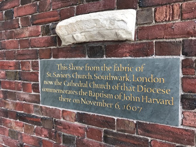 Wall of Memorial Church at Harvard. A piece of white stone is attached to the brick wall. The inscription below it reads: "This stone from the fabric of St. Savior's Church, Southwark, London, now the Cathedral Church of that Diocese commemorates the Baptism of John Harvard there on November 6, 1607.
