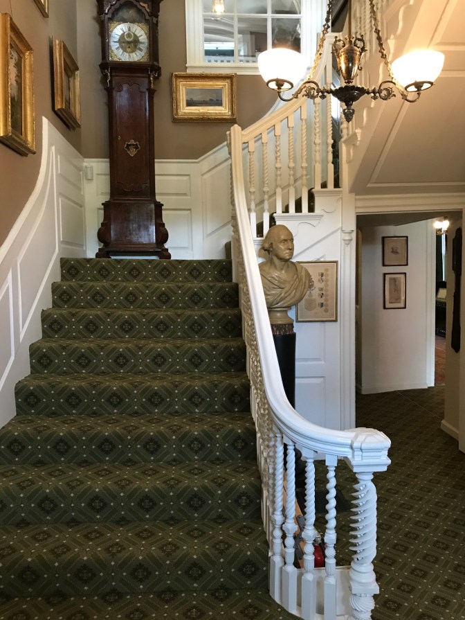 Main staircase. A grandfather clock is on the landing, and several paintings are on the walls.