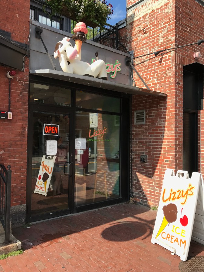 Exterior view of Lizzy's ice cream parlor. A white plastic cow lounges on the roof, holding an ice cream cone.