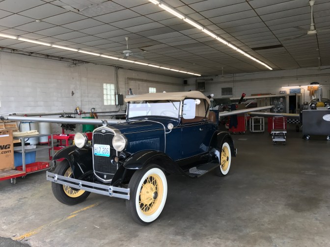 Airport hangar with a classic car and several airplanes being repaired.