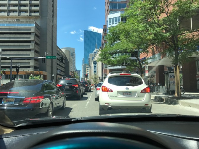 View from behind windshield of traffic in Boston. City buildings are in the background.