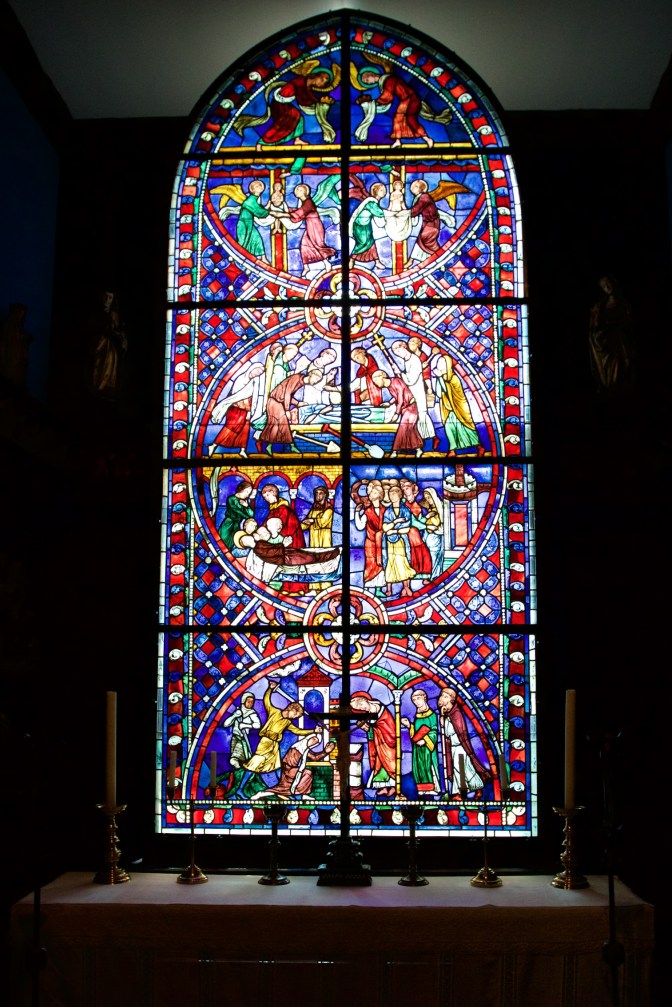 Stained glass window in front of altar table. A cross and several candles adorn the table.