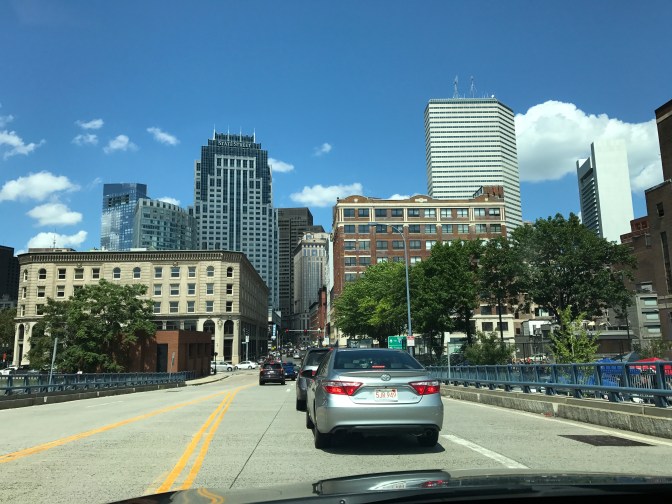 View of traffic and the Boston skyline from the driver's seat of a car.