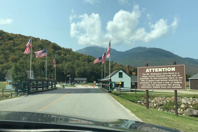Entrance to Mt. Washington Auto Road. Flags line the roadway, and the mountain peak is in the dance.