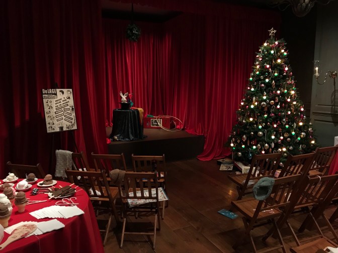 Christmas tree to the left of a stage. Two rows of wooden chairs are for the audience.