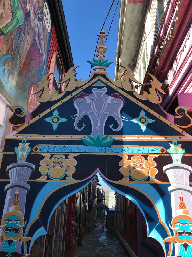 Decorated arch entrance to an alley. The arch says "Babydoll Gasoi Memorial Art Alley."