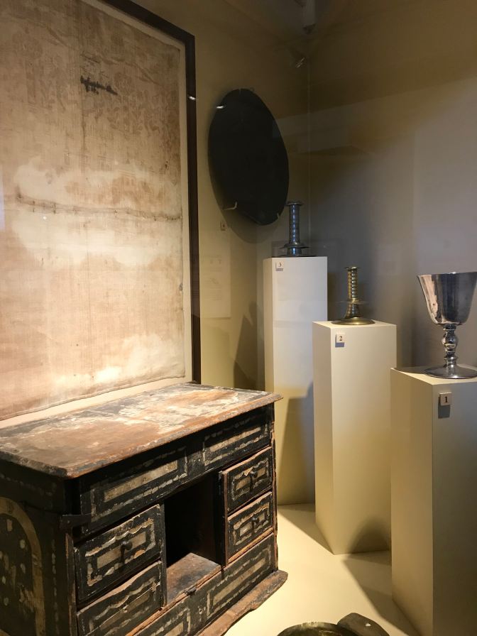 Objects from the Pilgrims include a writing desk, candle holders, a chalice, and a napkin.