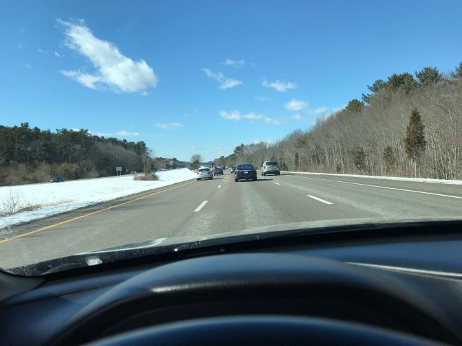 View from behind the wheel of a car on a highway. The sky is blue with a few clouds.