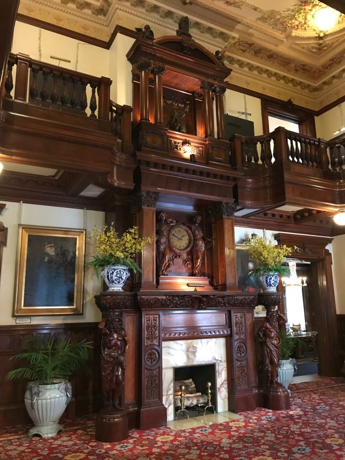 Elaborate wood and marble fireplace in center of living room of mansion.