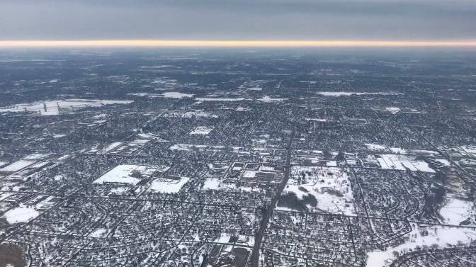 Sunrise on a cloudy day. View is from an airplane window, with the suburbs of Minneapolis in the foreground.