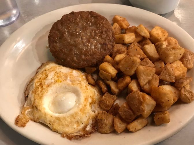 Plate of sausage and egg biscuit, with home fries.