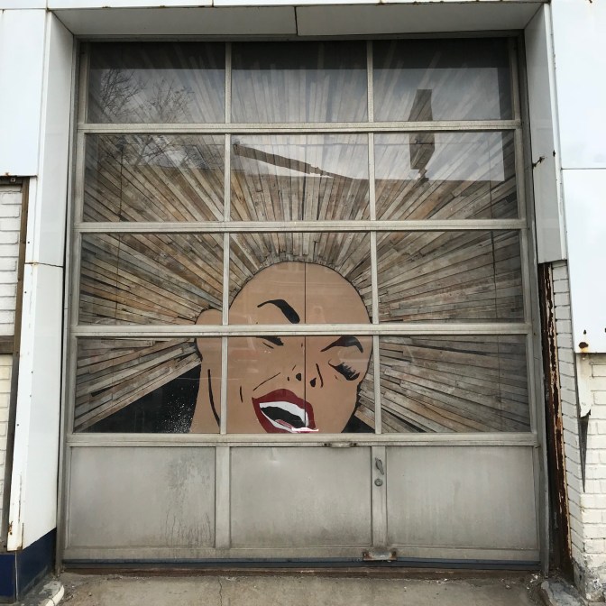 Garage door with painting of woman's face and hair made of wood extending in all directions.