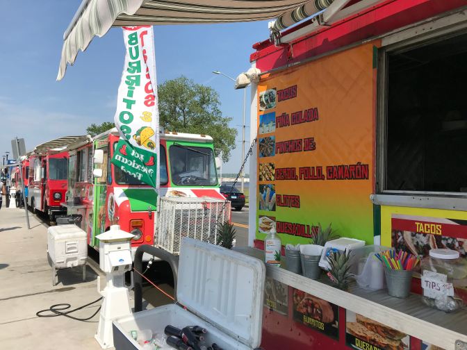 Food trucks at Food truck Paradise. The truck nearest to the camera has a menu of Mexican food items on its side.