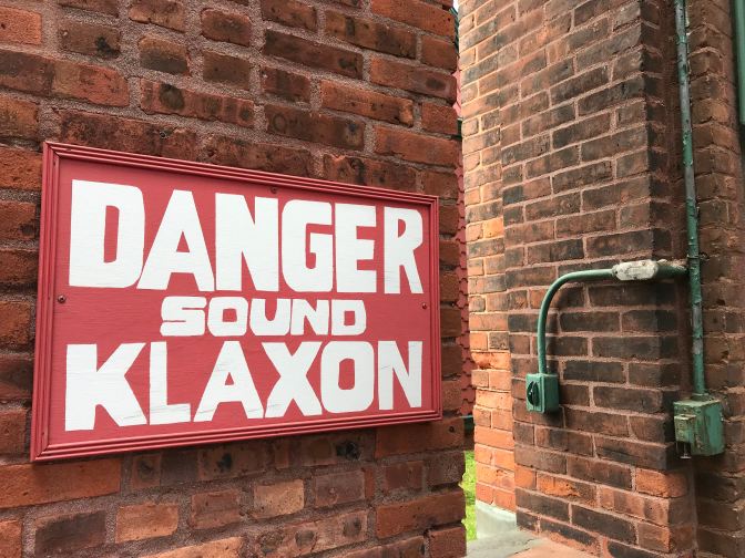Sign that reads DANGER SOUND KLAXON on a brick wall.