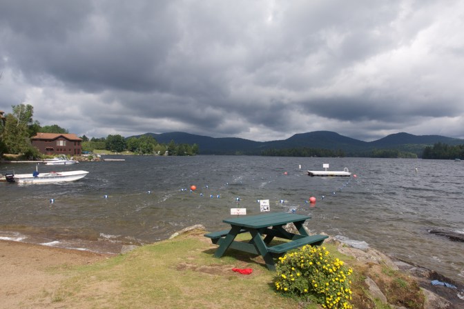 Photo of Blue Mountain Lake. A picnic bench is in the foreground on the beach.
