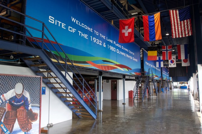 Flags hanging outside the arena, with a sign that says Welcome to the Lake Placid Olympic Center Site of the 1932 & 1980 Olympic Winter Games.