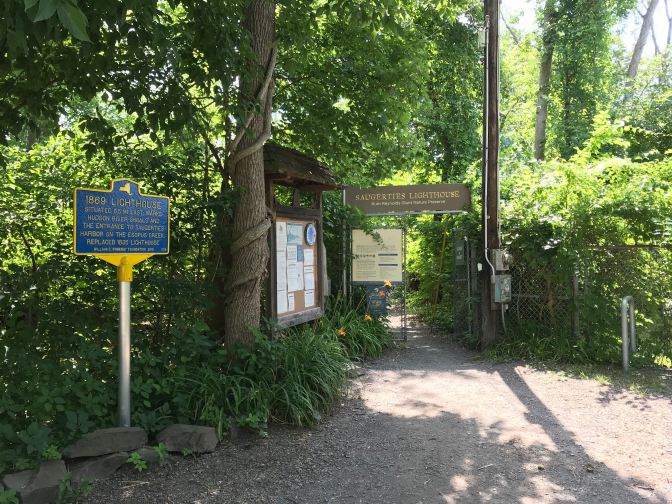 Entrance to the Saugerties Lighthouse park, through a chainlink fence in a wooded area.
