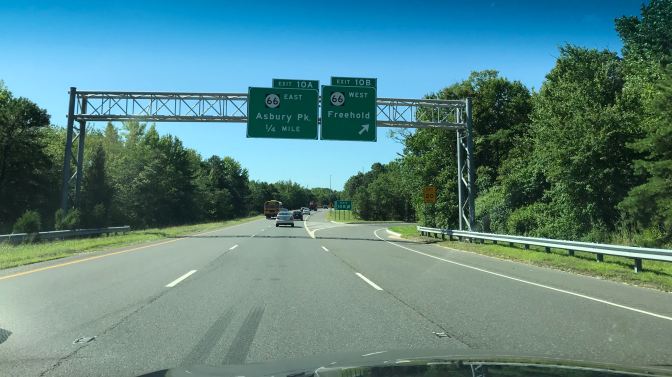 View of Route 18 from behind front windshield of car. A sign says Exit 10 B 66 West Freehold, Exit 10 A 66 East Asbury Park 1/4 Mile.