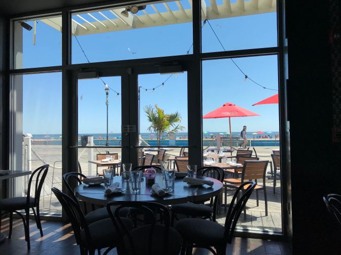 Empty table in front of window at restaurant that looks out to boardwalk and beach.