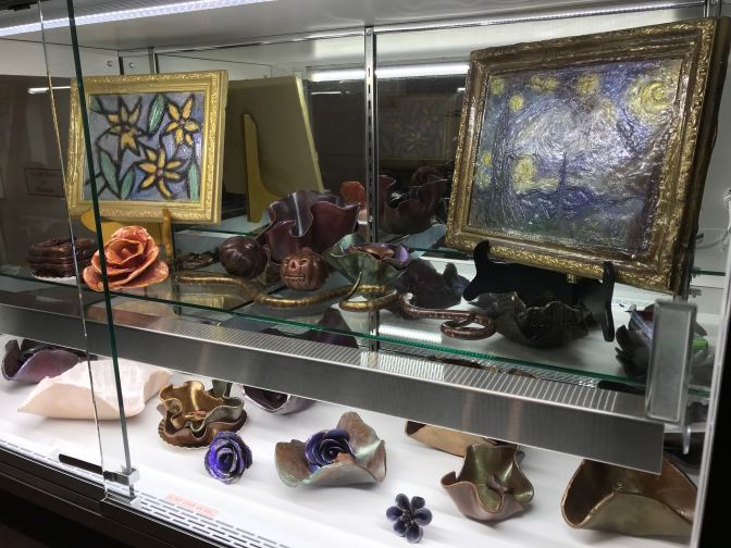 Display case of chocolate decorations, including chocolate paintings, bowls, flowers, and animals.