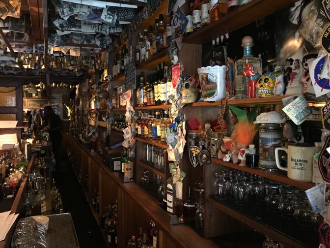 Taproom of The Dead Rabbits. Numerous whiskey bottles are on the shelves, and photographs hang from the ceiling.