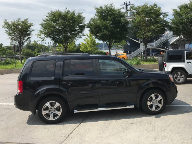 2012 Honda Pilot in black, pulling away from curb.