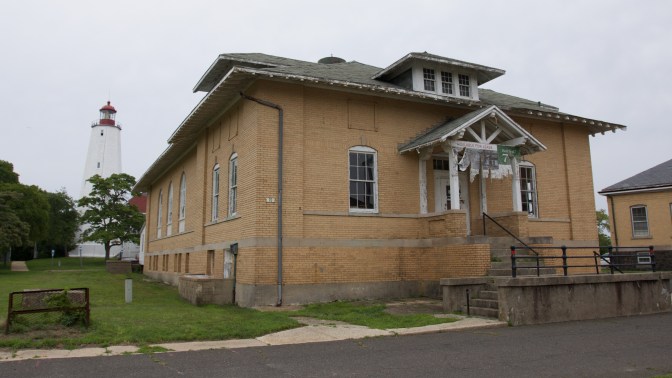 Building with tattered sign in foreground. The lighthouse is in the background.