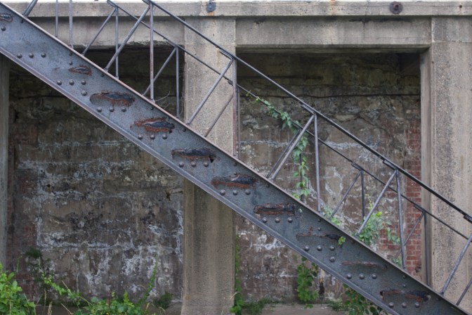 Rusty staircase in front of stone and brick wall.