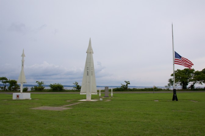 Nike-Hercules Missile system display, with two missiles in the foreground, beside an American flag at half staff.
