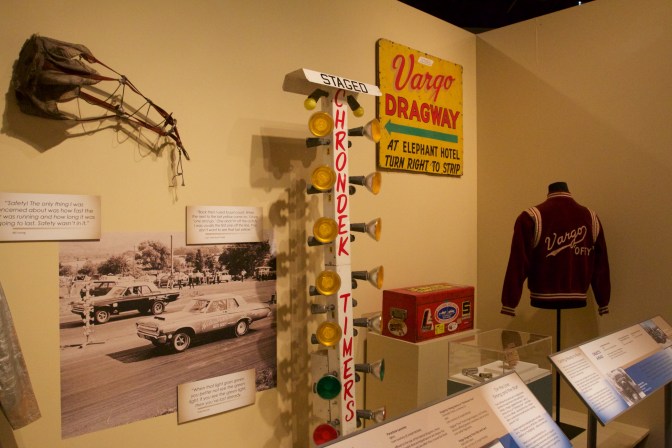 Exhibit of drag racing items from Cargo Dragway, including a parachute, a "christmas tree," a tool box, and a Cargo varsity jacket.