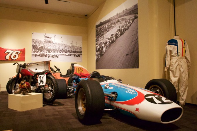 Two race cars and one racing bike in a corner of the exhibit.
