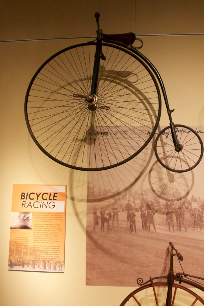 High Wheel Bicycle hanging from the ceiling in front of a display about bicycle racing.