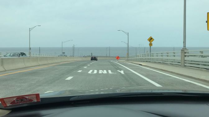 View of bridge through car windshield. The ocean is in the distance.