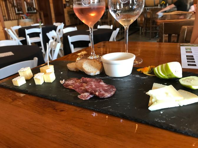 Two glasses of wine on a tabletop, with a cheese platter in the foreground.