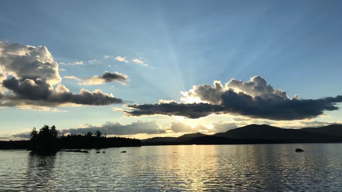 Sunset on Raquette Lake. Trees and mountains are in the distance.