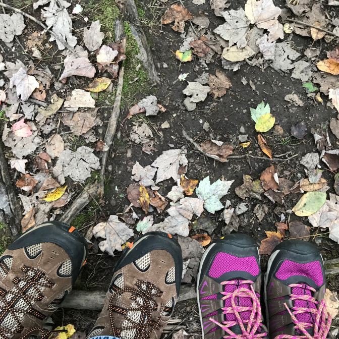 Two pairs of hiking shoes in the bottom of the image, standing on leaf-covered ground.