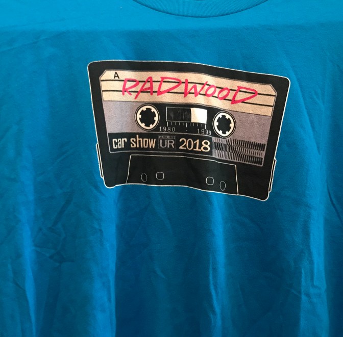 Blue t-shirt with image of cassette tape on front, with Radwood car show 2018 written on the tape.