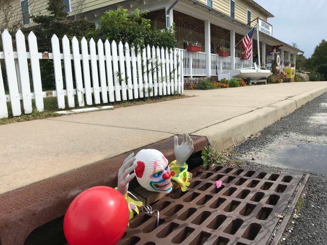 Clown's head, hands, and red balloon coming out of storm drain.