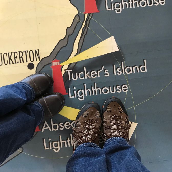 Floor map of NJ lighthouses. Two people's feet are in the photo near Tucker's Island Lighthouse.