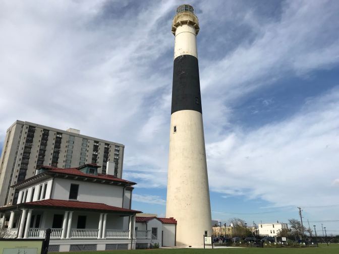Exterior of Absecon Lighthouse, with the lighthouse keeper's residence to the left. A high rise apartment building is in the background.