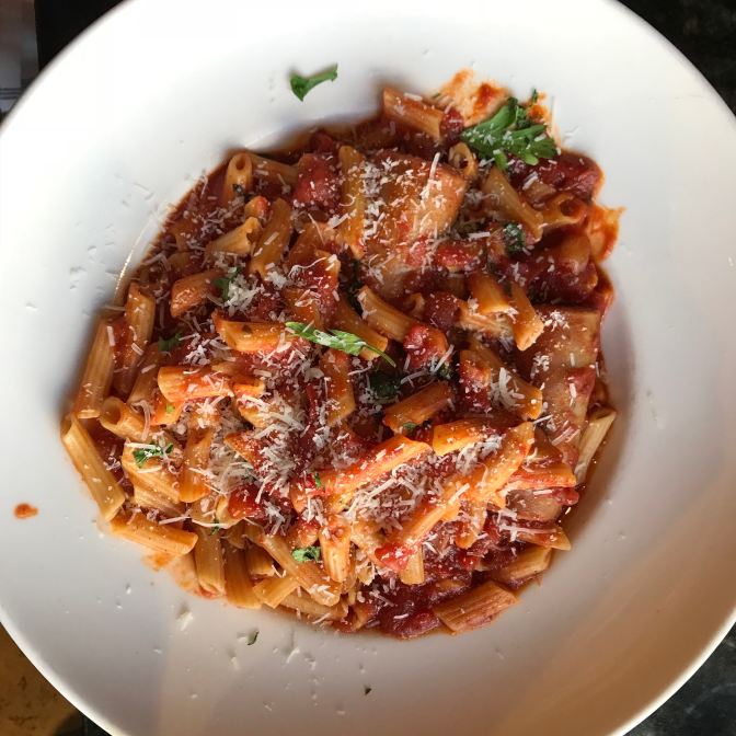 Sausage and pasta with red sauce, on a white plate.