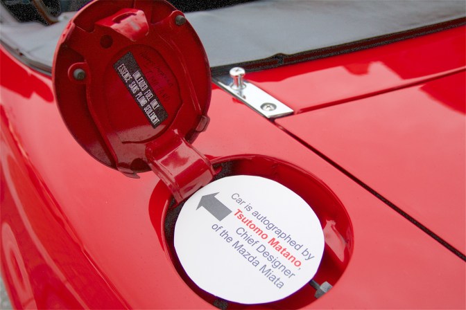 Red Mazda Miata gas cap with signature of Tsutomo Matano, chief designer of the Miata.