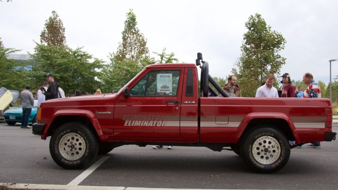 Red Jeep Comanche Eliminiator pickup truck. Spectators mill around it.