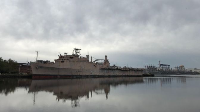 View of the USS Nashville moored at the Navy Yard. Other ships, as well as cranes, are in the background.