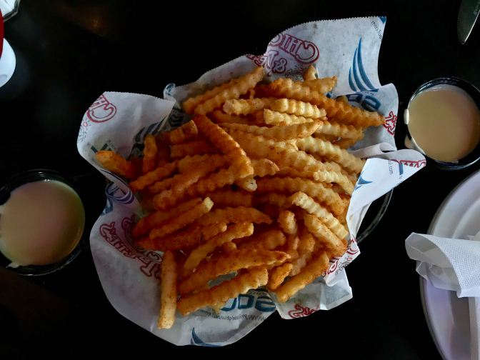 Basket of crab fries, with two containers of cheese dip on either side.